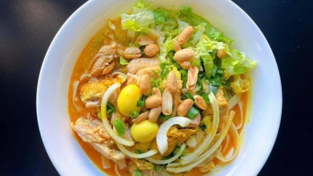 A white bowl with a yellow broth dish, featuring leafy greens, nuts, and onions.
