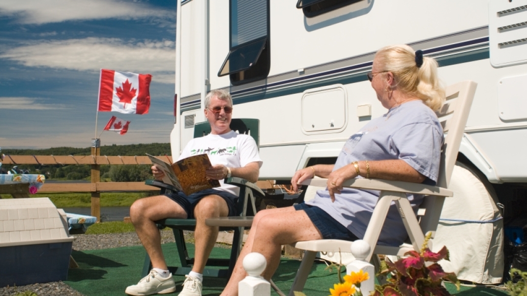 Smiling elderly couple sits on lawn chairs in front of an RV.