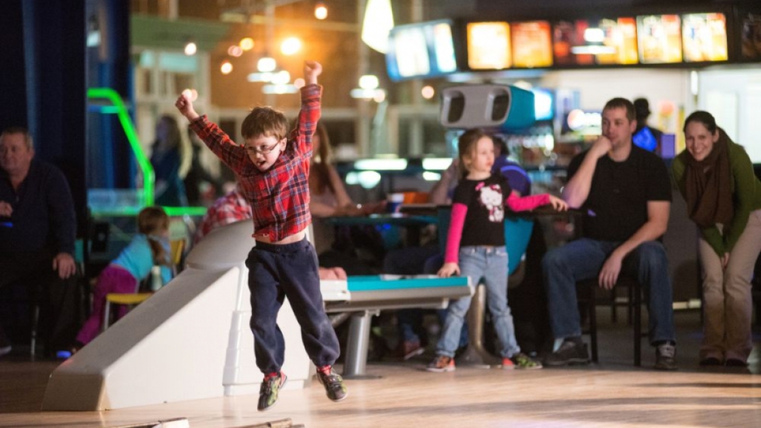 Child with glasses jumpin with excitement at bowling alley