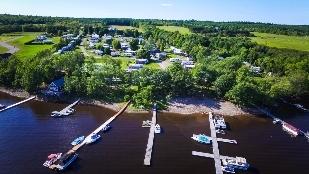 aerial shot of a dock on a river with boats and a lush green camping site behind it