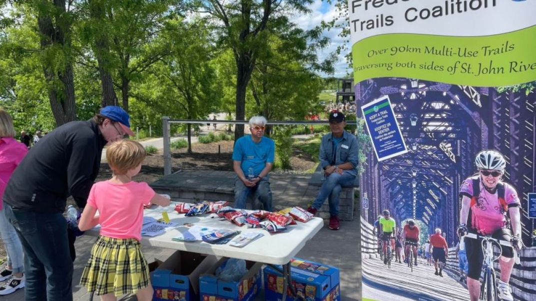 people around a plastic table with snacks on it with a sign that talks about the trails on the side