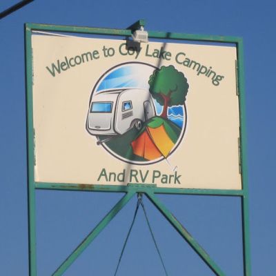 Coy Lake Camping sign featuring their logo, which is a graphic of an RV, a tree and an orange tent