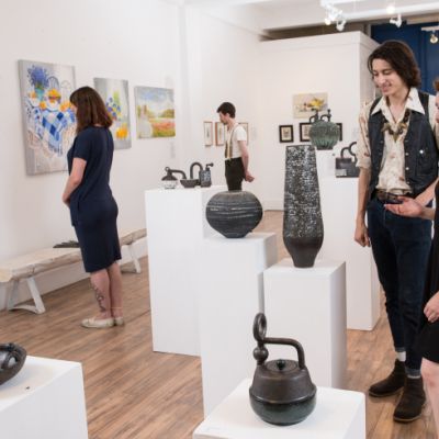 four people in a gallery viewing colourful paintings and black pottery