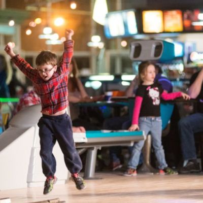 Child with glasses jumpin with excitement at bowling alley