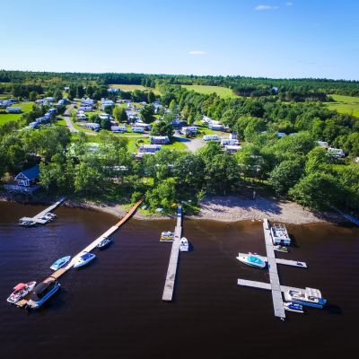 aerial shot of a dock on a river with boats and a lush green camping site behind it