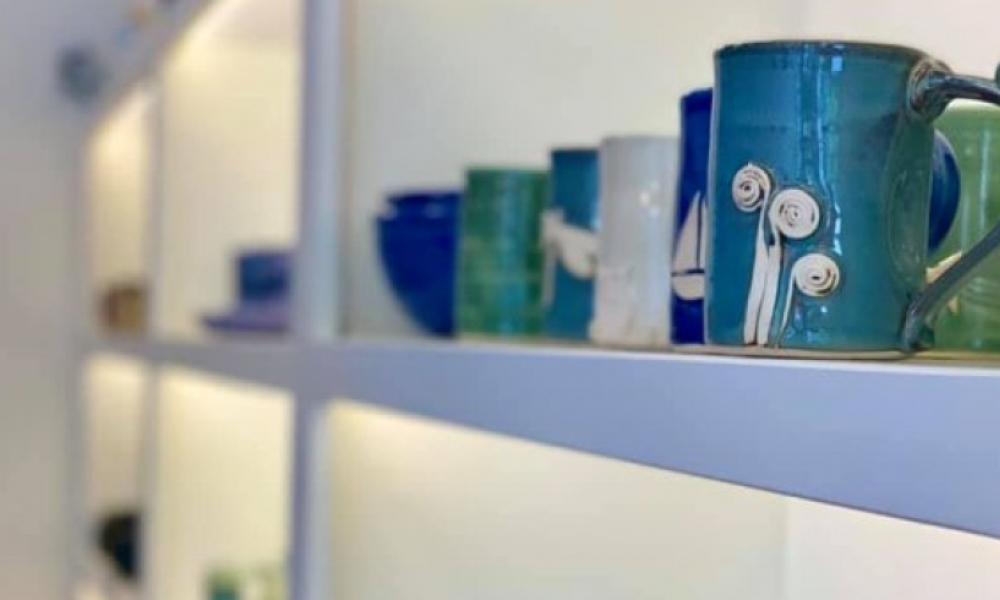 close up shot of pottery mugs and bowls on a white shelf