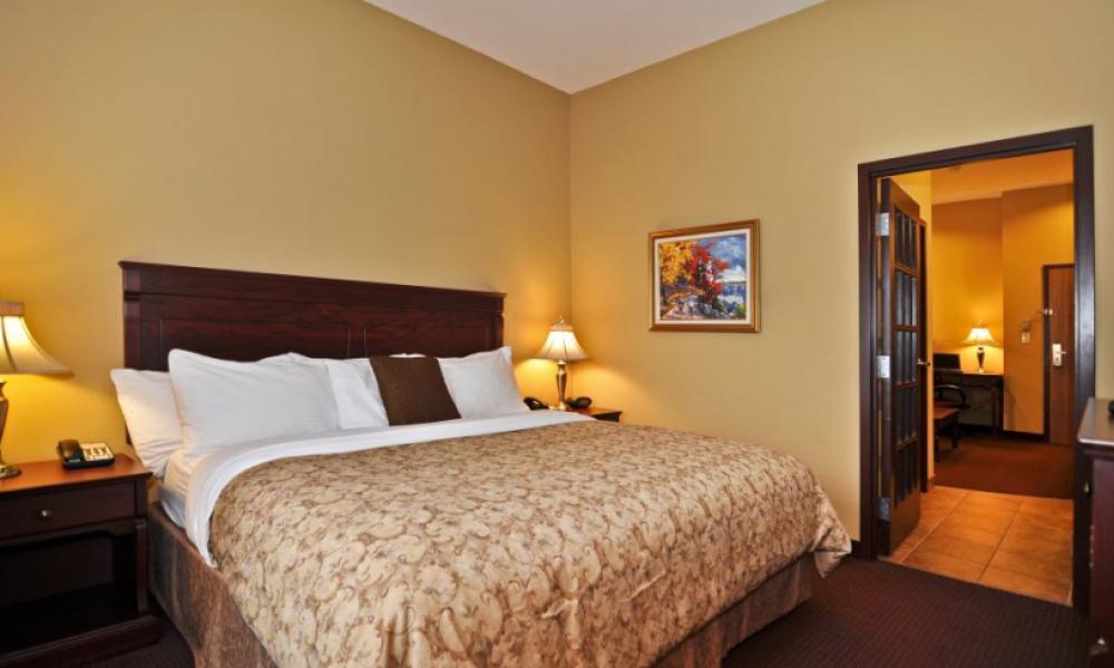 Interior shot of a hotel room with a king bed. Beige walls and dark trim. 