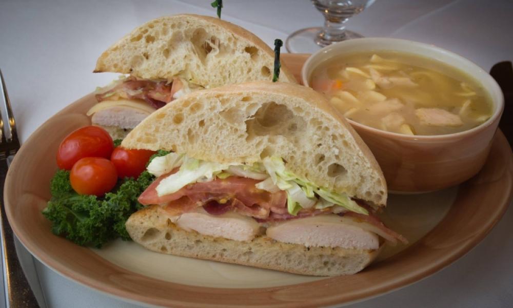 a club sandwich with soup on a pink and beige plate