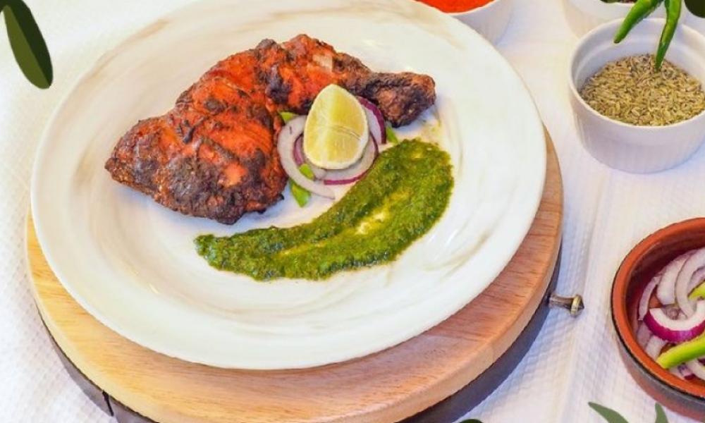 a white plate with a baked chicken leg and a pesto sauce