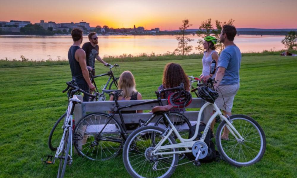 Group of people with bikes sitting on a park bench overlooking the water and city skyline