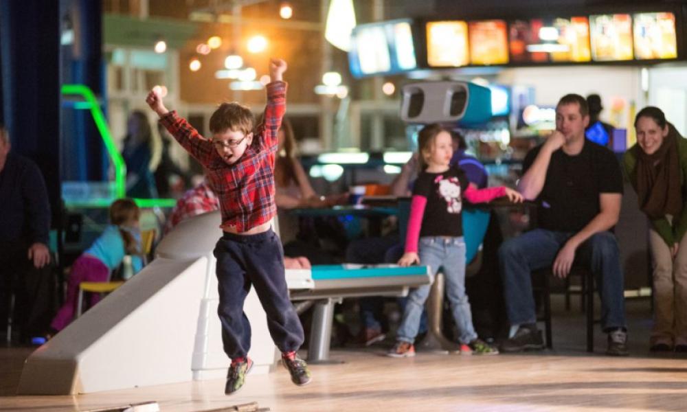 Child with glasses jumpin with excitement at bowling alley