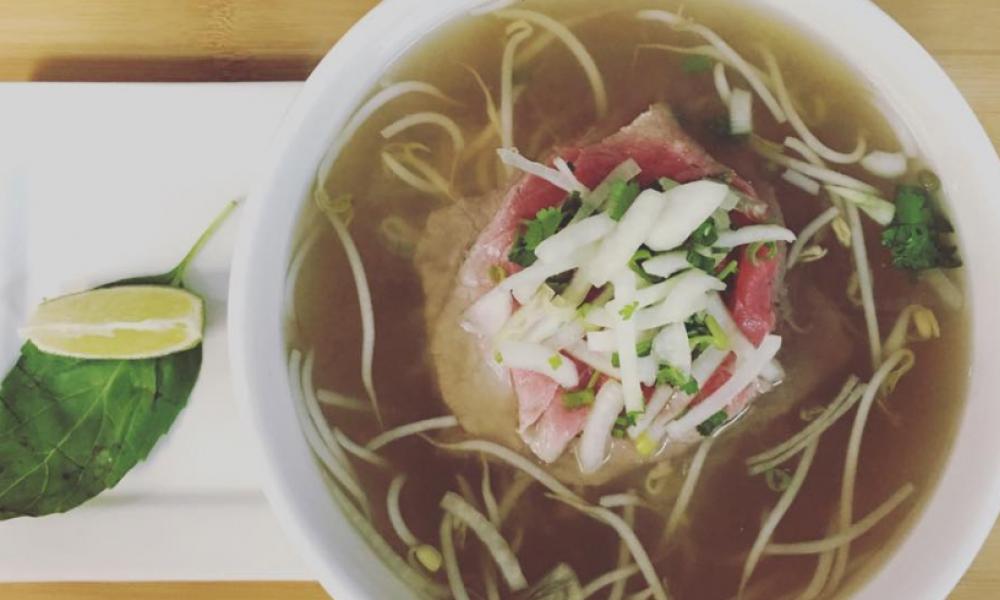 White bowl of noodle and meat in broth on a table