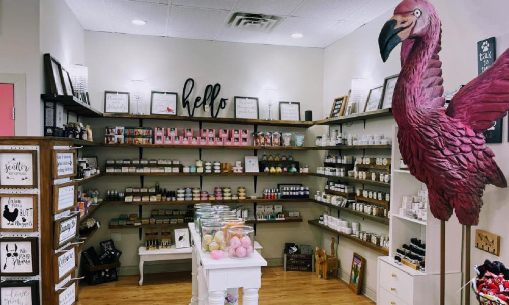 picture of Whimsy store with a right pink flamingo statue in the foreground with its wings stretched and shelves full of product in the background